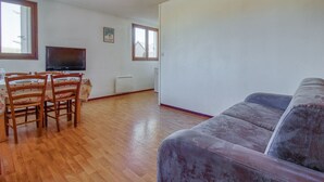 Un salon avec un plancher en bois, un canapé violet, une table à manger avec des chaises, un téléviseur et une affiche accrochée au mur.
