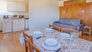 Un espace de vie compact comprenant un coin repas pour quatre personnes, une kitchenette et un canapé gris.