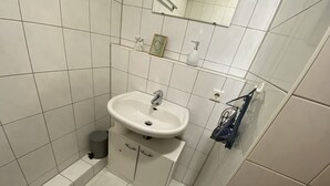 Une salle de bain avec un lavabo blanc, un miroir et une petite poubelle.