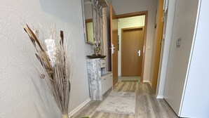 Un couloir avec un plancher en bois, un tapis vert et noir, une plante et un miroir posé sur un meuble.