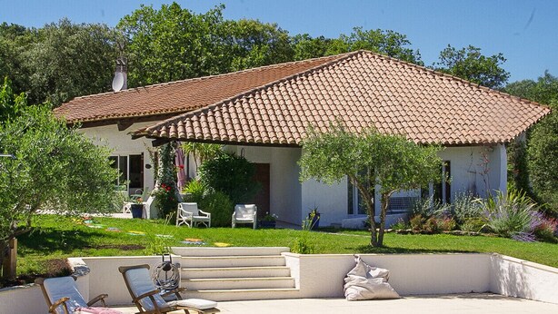 Una casa con techo de tejas, piscina y mobiliario exterior.