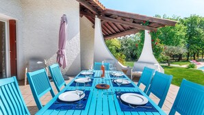 Un espacio de comedor al aire libre con una mesa dispuesta para seis personas, sillas azules y una pérgola en la parte superior.