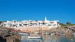 Un pueblo costero con edificios blancos, costa rocosa y barcos en el agua.