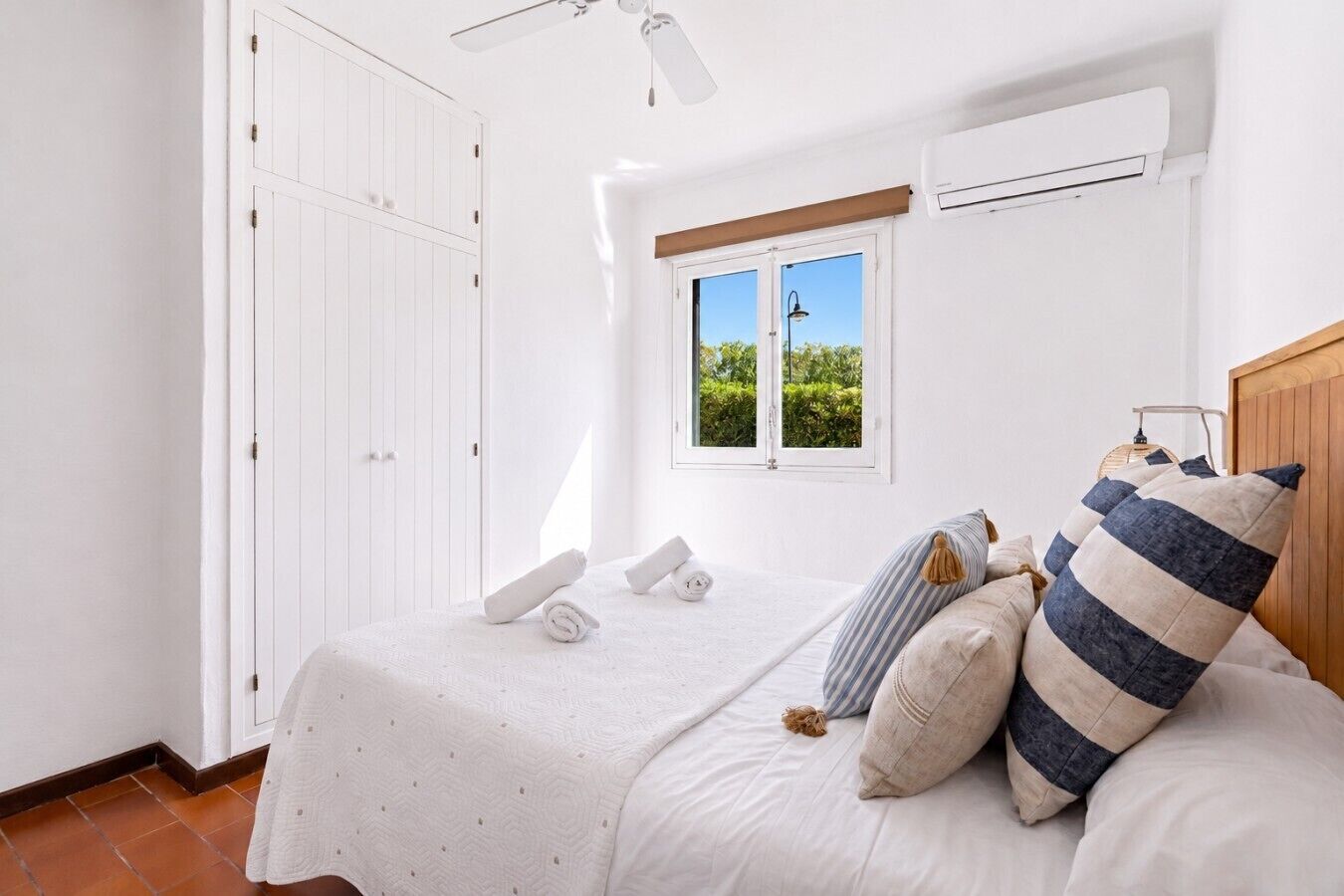 A bedroom with a bed, pillows, a window, and an air conditioning unit.