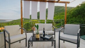 Una terraza con dos sillas blancas acolchadas, una mesa de vidrio con una planta de cactus y una botella de vino.