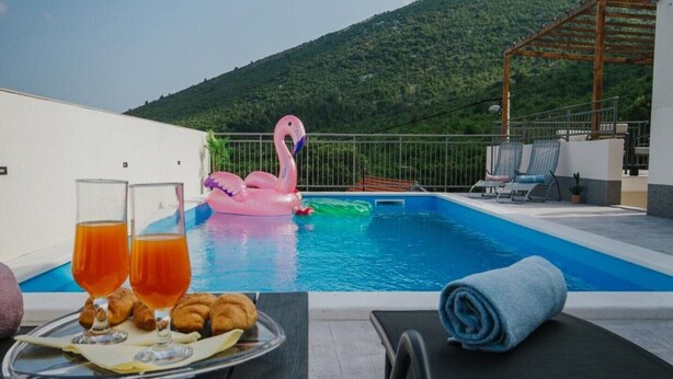 Escena junto a la piscina con un flotador de flamenco, una mesa con bebidas y pasteles, y sillones de descanso.