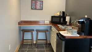 Una cocina compacta con microondas, cafetera y dos taburetes.