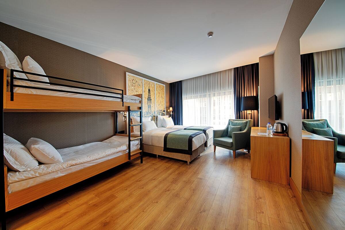 A hotel room with a bunk bed, a single bed, a desk with a chair, and a television.