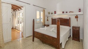Un dormitorio con una cama de madera con dosel, una mesita de noche pequeña, una mesita auxiliar y un estante con adornos.
