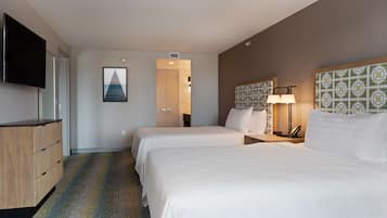 A hotel room with two beds, a TV, a desk with a lamp, and a patterned headboard.