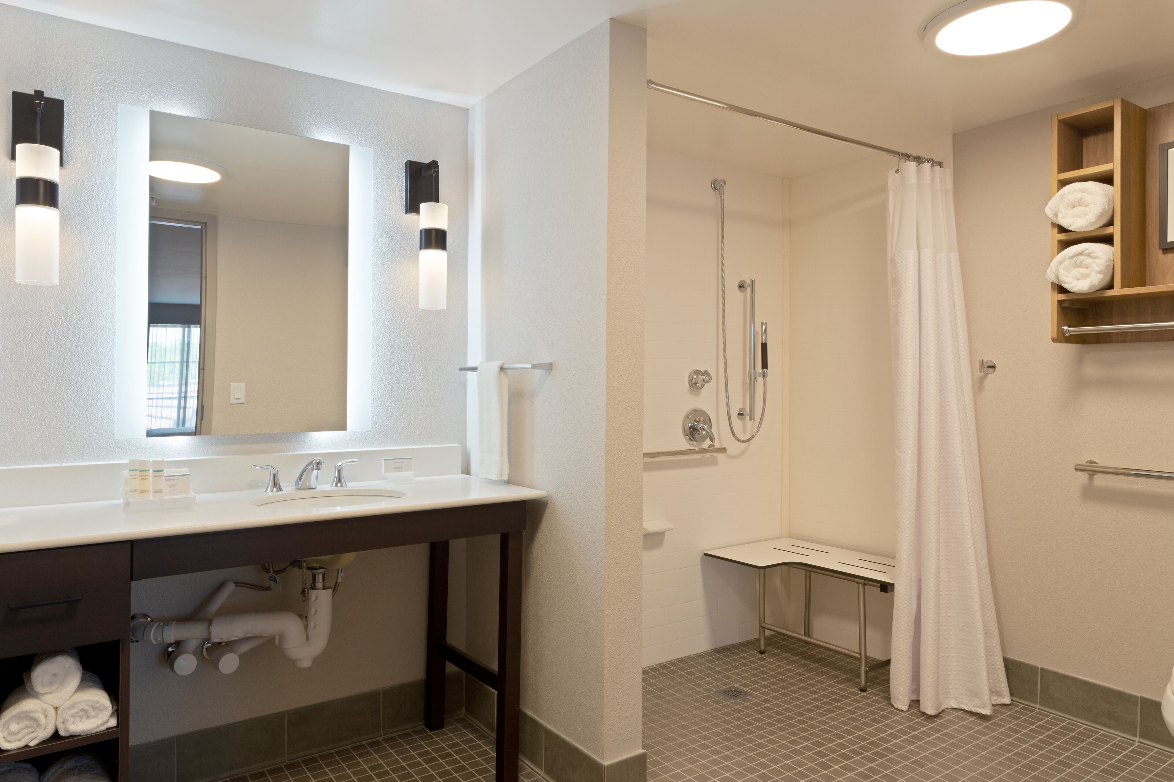 Ein modernes Badezimmer mit großem Spiegel, Waschbecken, Dusche und Handtuchhalter.