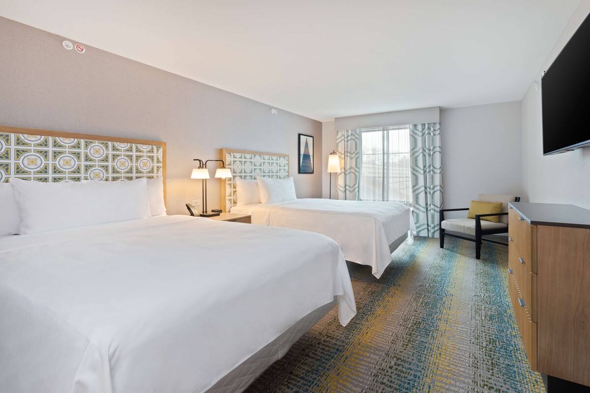 A hotel room with two beds, a desk, a chair, a TV, and a window with curtains.