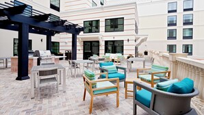 An outdoor patio with wicker furniture, a grill, and a view of the building's interior. - Homewood Suites by Hilton St. Augustine San Sebastian (St. Augustine)