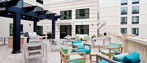 An outdoor patio with wicker furniture, a grill, and a view of the building's interior.