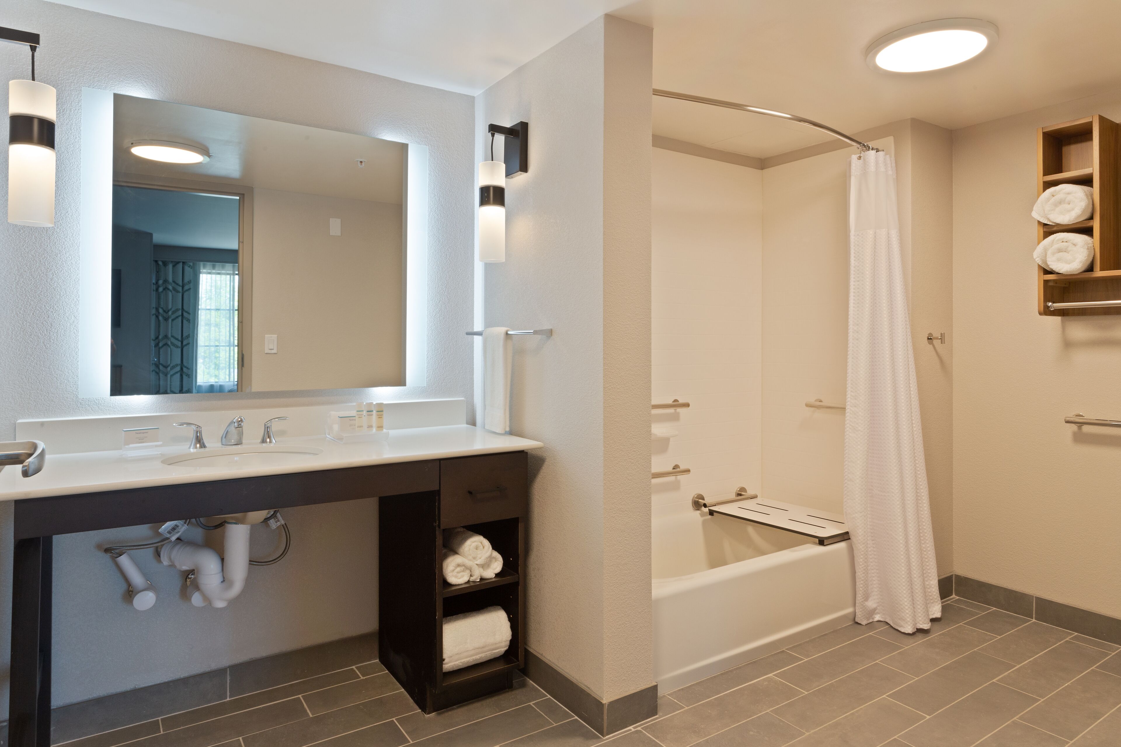 A modern bathroom with a large mirror, dual sinks, a shower, and a towel rack.