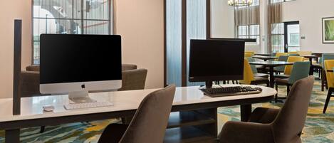 A hotel room with two Apple iMac computers on a desk, a chair, and a large window with curtains.