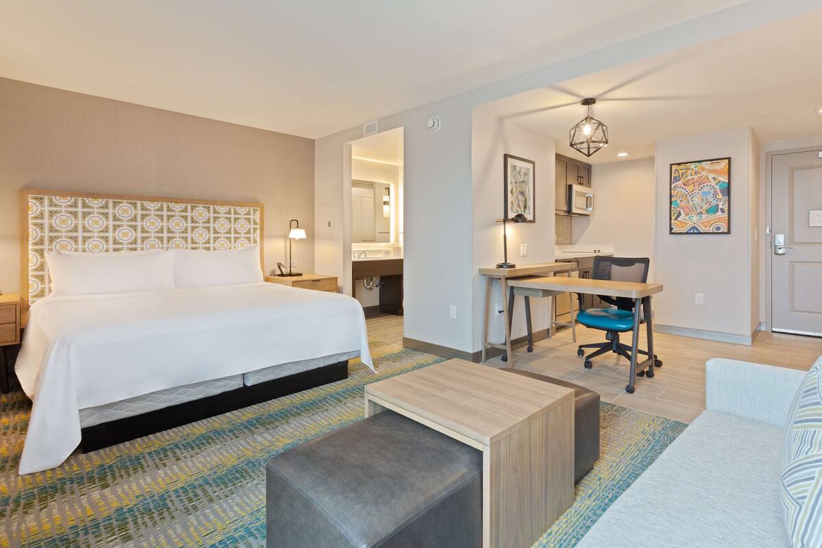 A hotel room with a large bed, a desk, a chair, a sofa, and a small table.