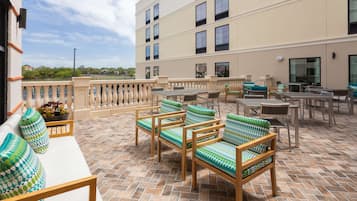 A terrace with outdoor seating, a view of the city, and a building with multiple windows.