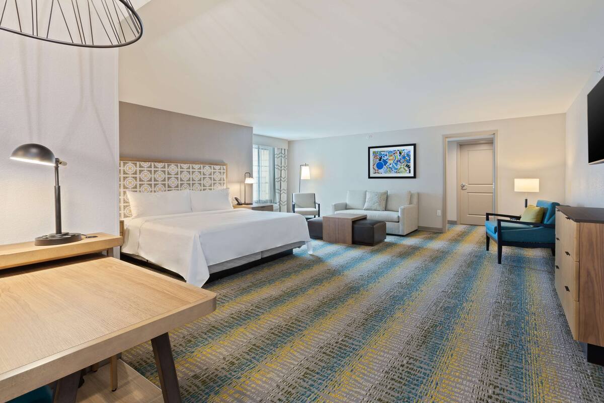 A hotel room with a bed, a desk, a sofa, a TV, and a patterned carpet.