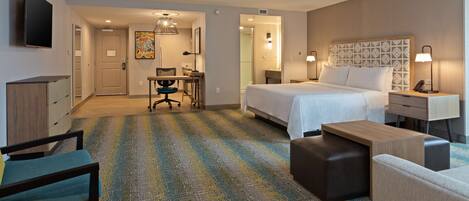 A hotel room with a bed, a desk, a chair, a TV, and a bathroom visible through an open door.