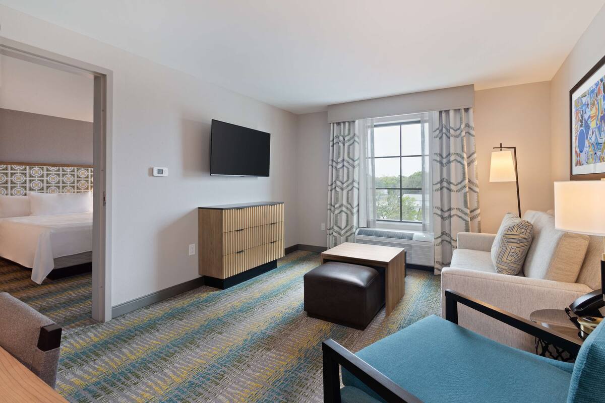 A hotel room with a bed, a desk, a sofa, a TV, and a window with curtains.