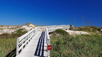 A wooden boardwalk leading to a beach with a red bicycle sign.