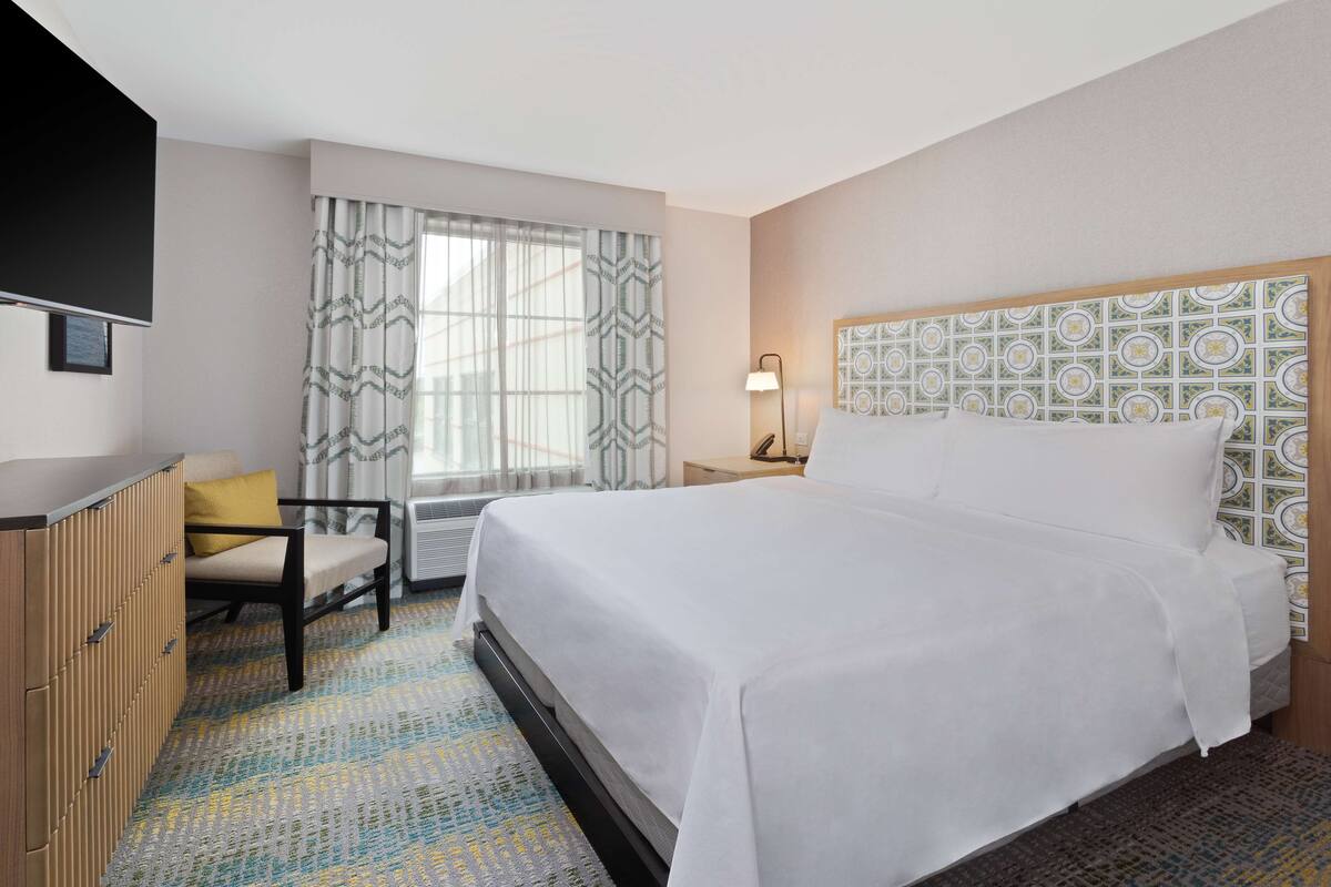 A hotel room with a bed, a desk, a chair, and a window with curtains.