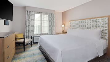 A hotel room with a bed, a desk, a chair, and a window with curtains.
