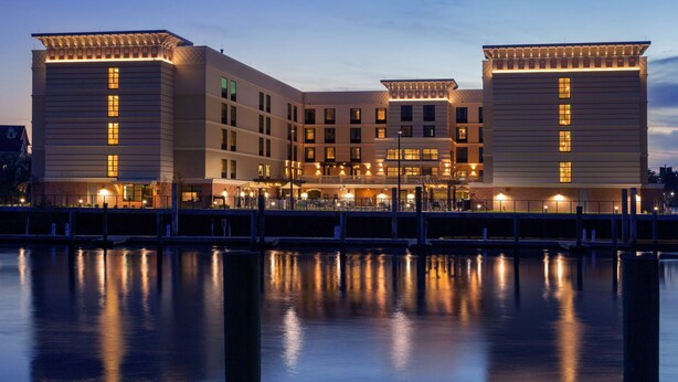 A multi-story hotel with a waterfront view, featuring a reflective pool in front. - Homewood Suites by Hilton St. Augustine San Sebastian (St. Augustine)