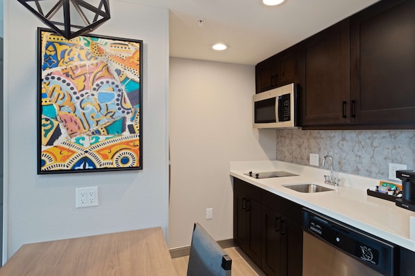 A modern kitchen with dark cabinets, a double sink, and a microwave.