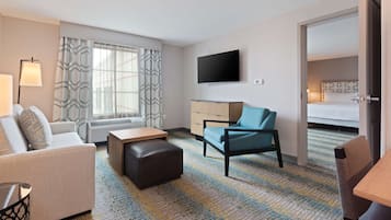 Ein Hotelzimmer mit einer Couch, einem Sessel, einem kleinen Tisch, einem Fernseher und einem Bett.