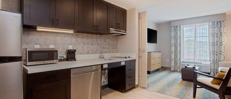 A modern kitchen with dark cabinets, stainless steel appliances, and a marble backsplash.