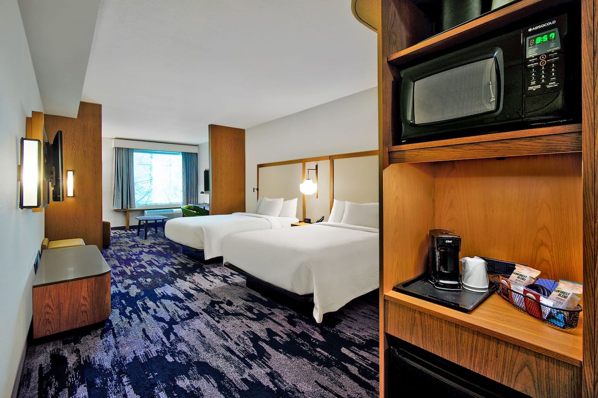 A hotel room with two beds, a microwave, a coffee maker, and a small seating area.