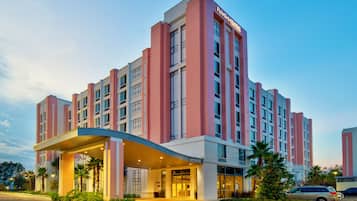 A multi-story hotel with a prominent entrance, large windows, and a covered area with palm trees.