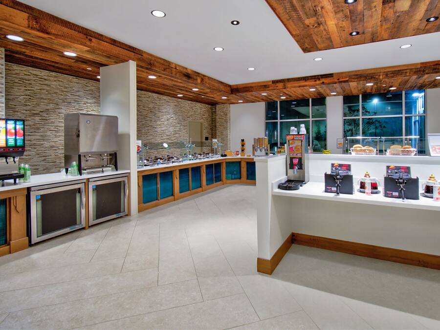 A modern breakfast area with a stone wall, wooden ceiling, and a variety of food and beverage dispensers.