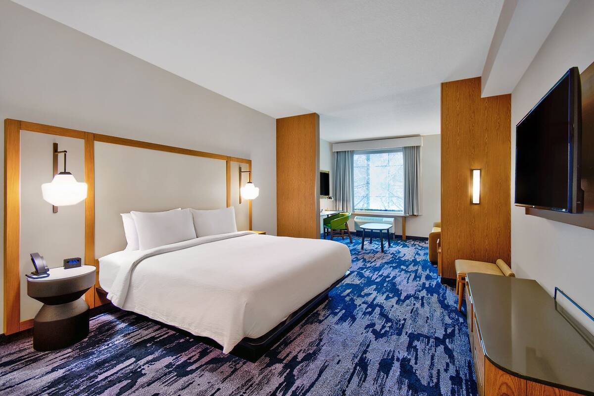 A hotel room with a large bed, a desk, a chair, a TV, and a window with curtains.