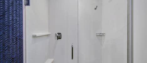 Une douche à l’italienne avec une porte en verre, un pommeau de douche amovible et un distributeur de serviettes fixé au mur.