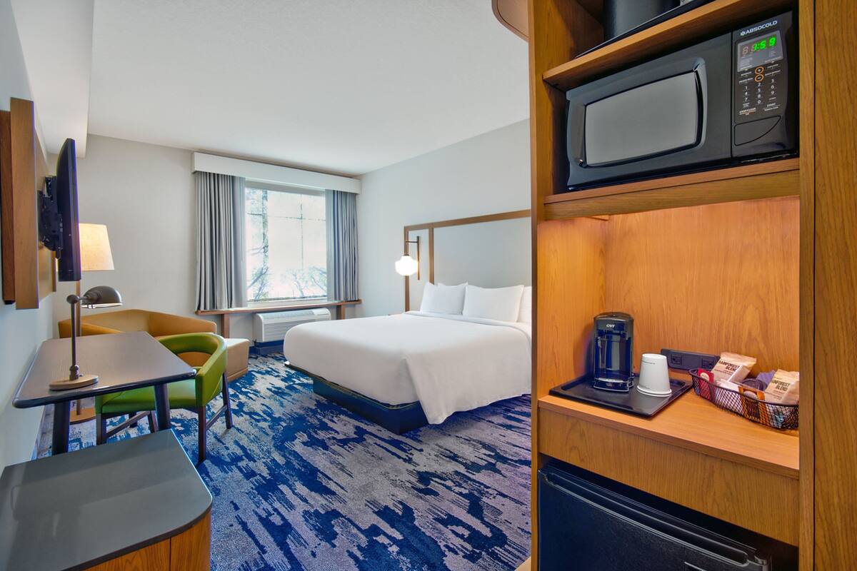 A hotel room with a bed, a desk, a chair, a microwave, and a coffee maker.