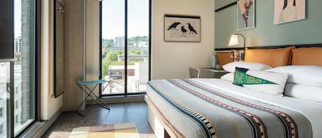 Habitación de hotel moderna con una cama grande, una mesita, una silla y vistas a la ciudad por la ventana.