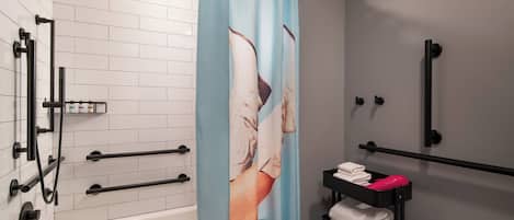 Un baño moderno con pared de azulejos blancos, ducha con manguera negra, toallero con toallas y cortina de ducha con una imagen parcial de una persona.