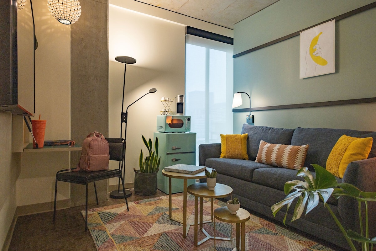 A modern living room with a sofa, a small table, a chair, a floor lamp, a radiator, and a potted plant.