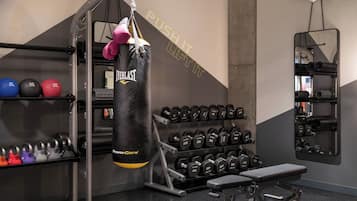 A gym with a punching bag, various weights, and a bench.