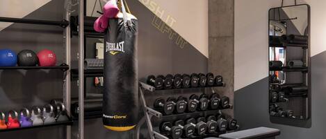 Un gimnasio con un saco de boxeo, pesas variadas y un banco.