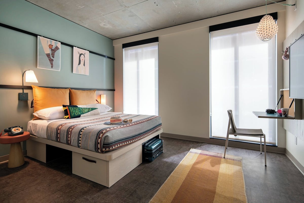A modern bedroom with a bed, bedside table, lamp, and a large window.