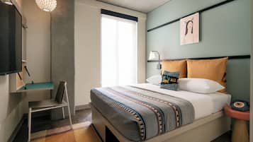 A modern bedroom with a bed, a desk, a chair, a lamp, and a wall-mounted artwork.
