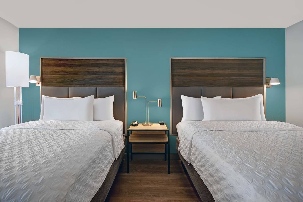 A hotel room with two beds, a nightstand, and a lamp.