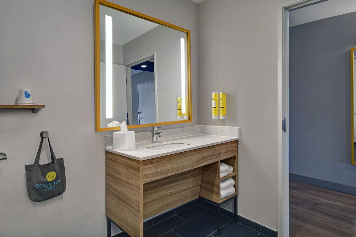 A modern bathroom with a wooden vanity, a large mirror, and a towel shelf.