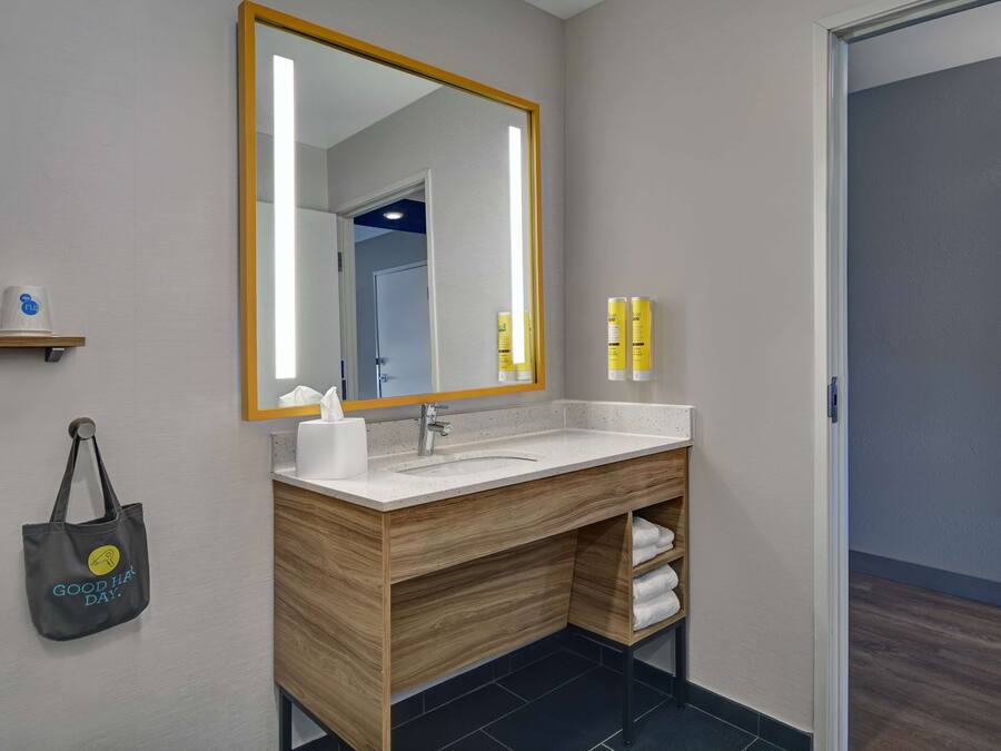 Un baño moderno con un mueble de tocador de madera, un espejo grande y un estante para toallas.