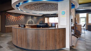 Un área de recepción de hotel moderna con un mostrador curvo de madera, una pantalla digital y una pared decorativa con un diseño de círculos.