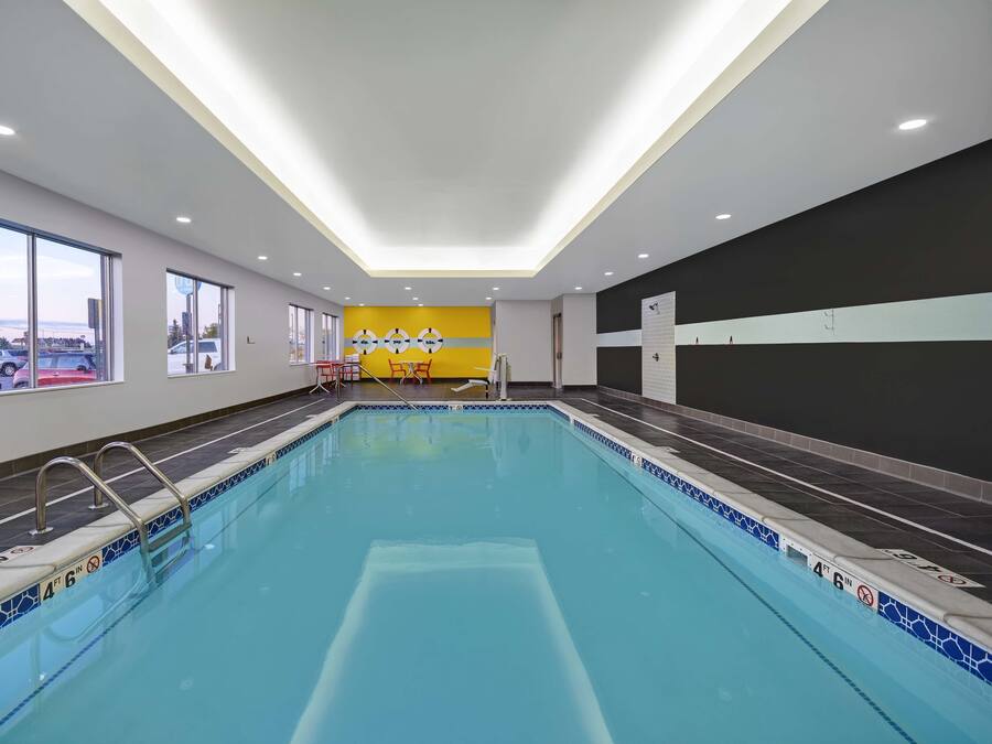 A modern indoor swimming pool with clear lane markings, a tiled edge, and a view of the outside through large windows.